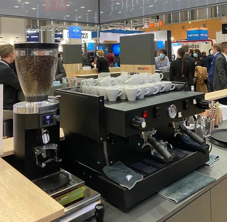 Schwarze La-Marzocco-Siebträgermaschine mit Mahlkönig-Mühle und vorgewärmten Tassen