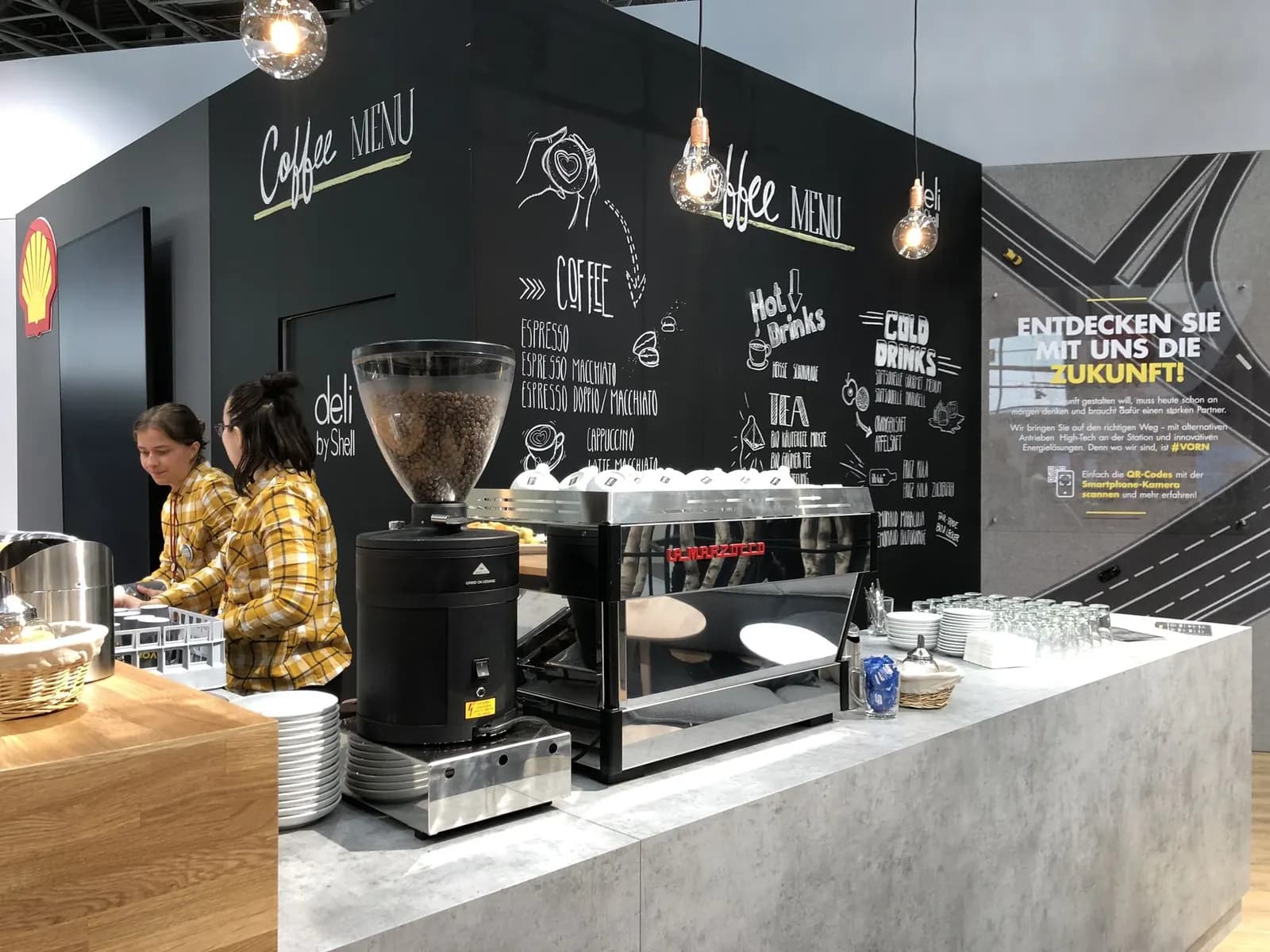 Kaffeebar mit Siebträgermaschine und Mühle vor einer Menütafel an einem Messestand